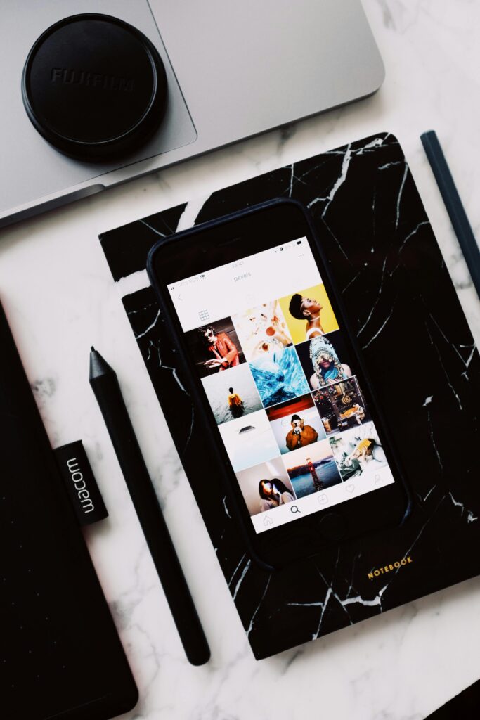 Black organizer with mobile phone app demonstrating creative images on screen and cup located on laptop touch pad near marker put on marble table